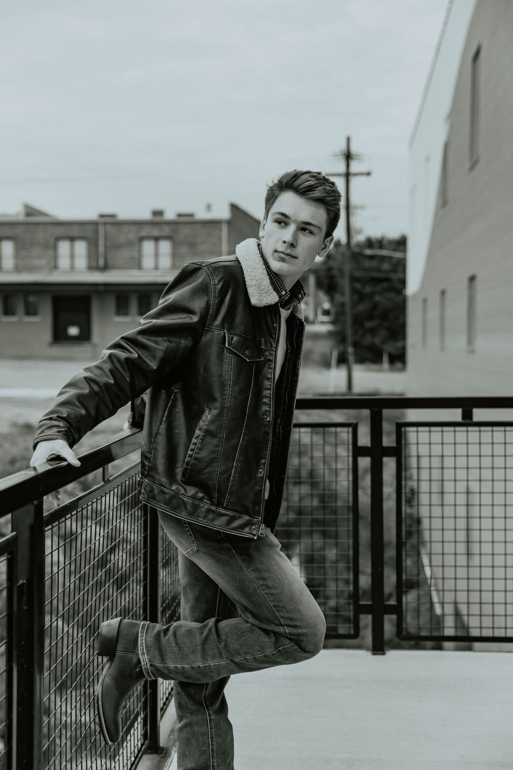 Black and white portrait series leaning on metal railing in casual denim jacket.
