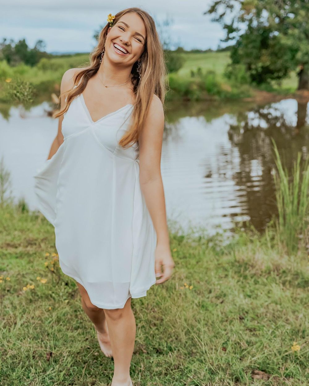 Summer portrait by lake wearing flowing white dress in natural setting.