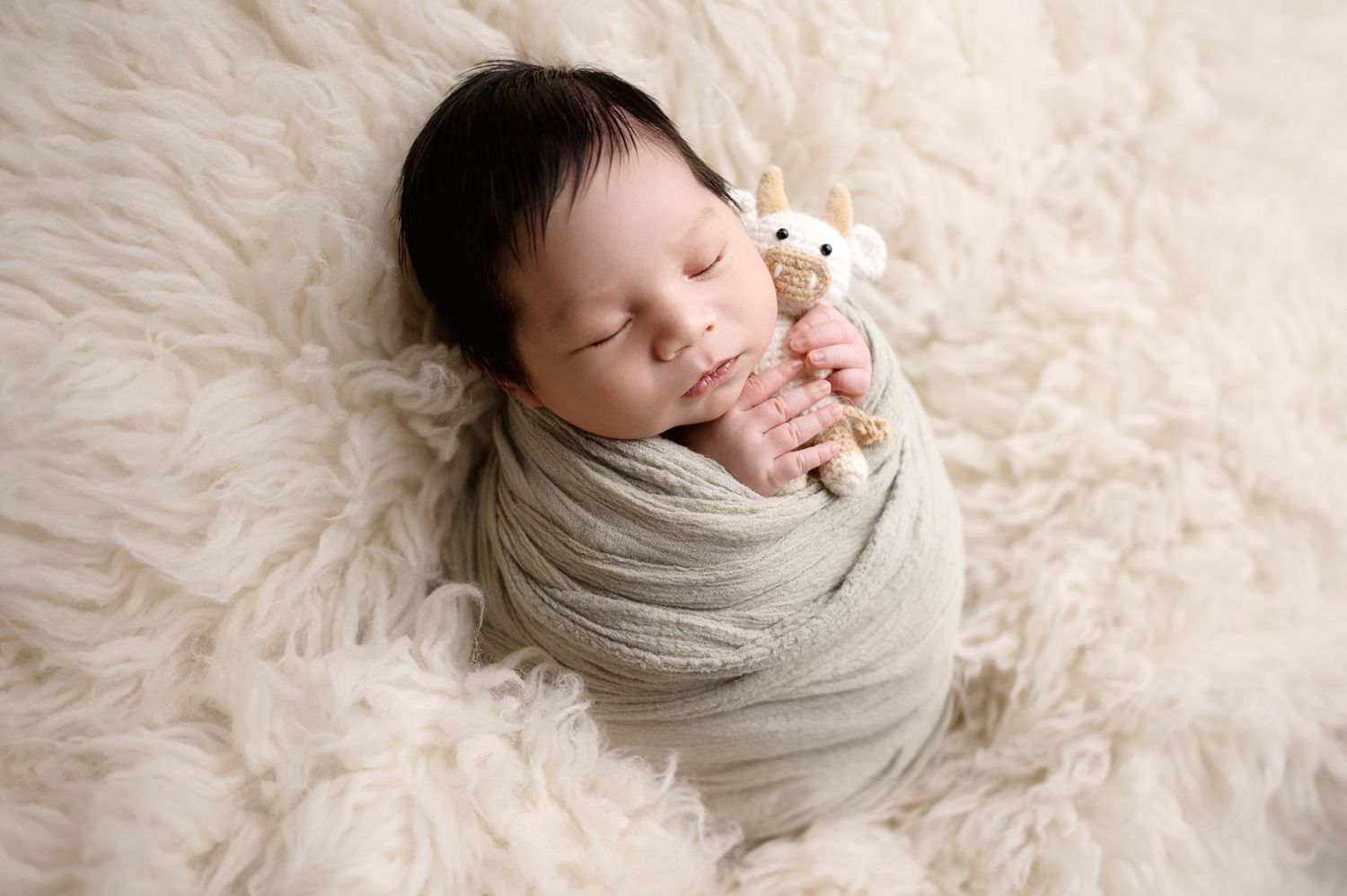Peaceful sleeping newborn wrapped in soft beige swaddle on fluffy white rug.
