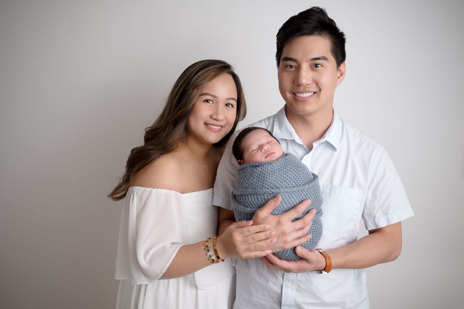 Family of three posing together against white backdrop in studio setting.
