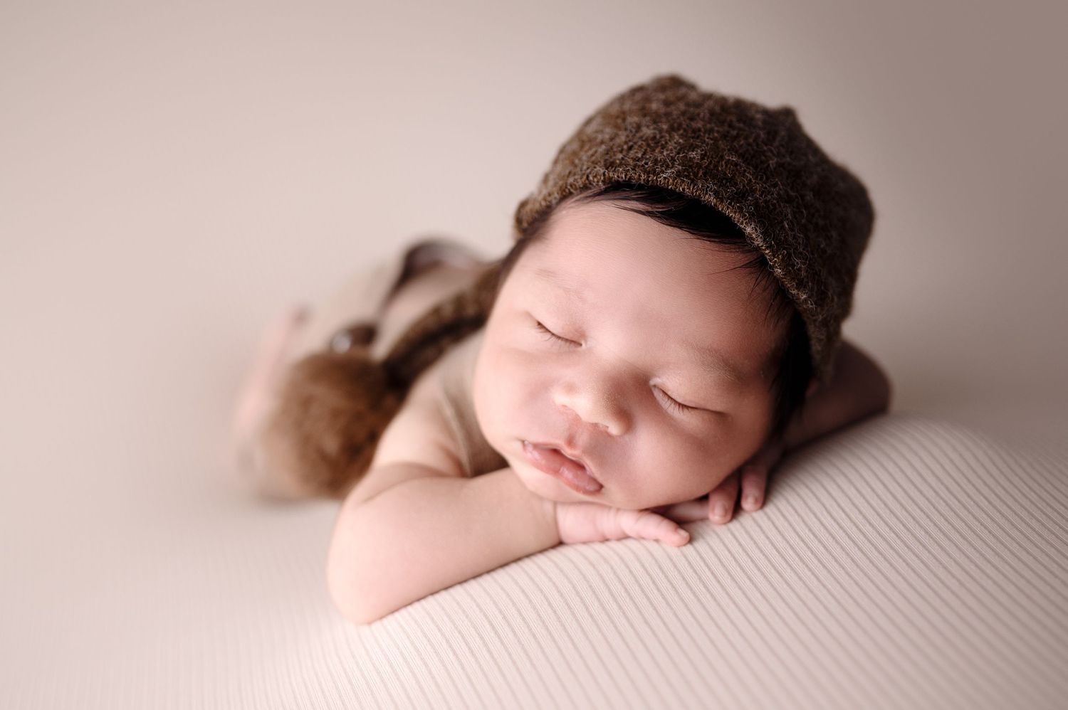 Sleeping newborn wearing brown cap resting on white textured surface.
