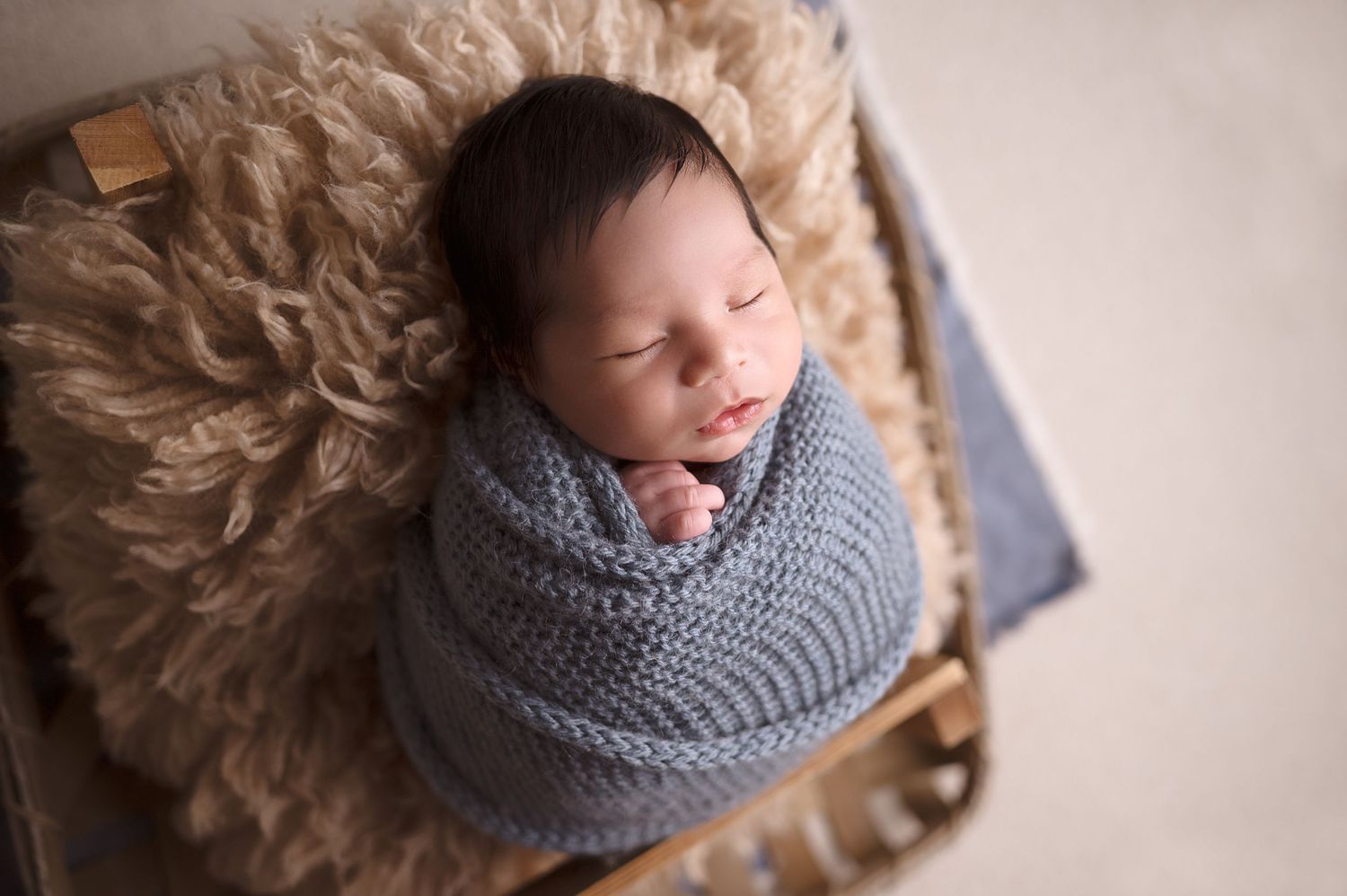 Peaceful newborn baby sleeping in gray knit wrap on soft textured surface.