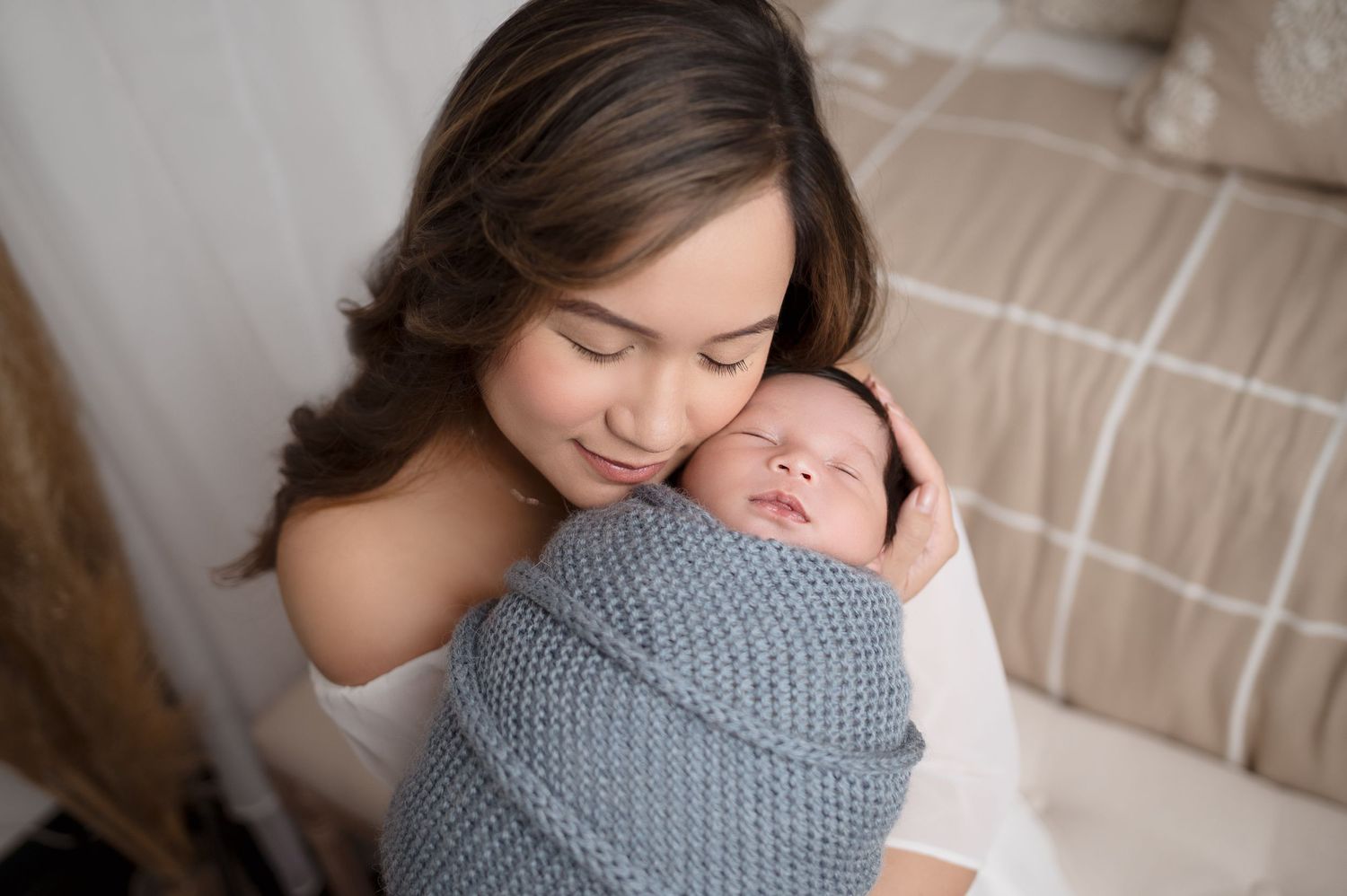 Mother and baby sharing intimate moment on beige bedding.