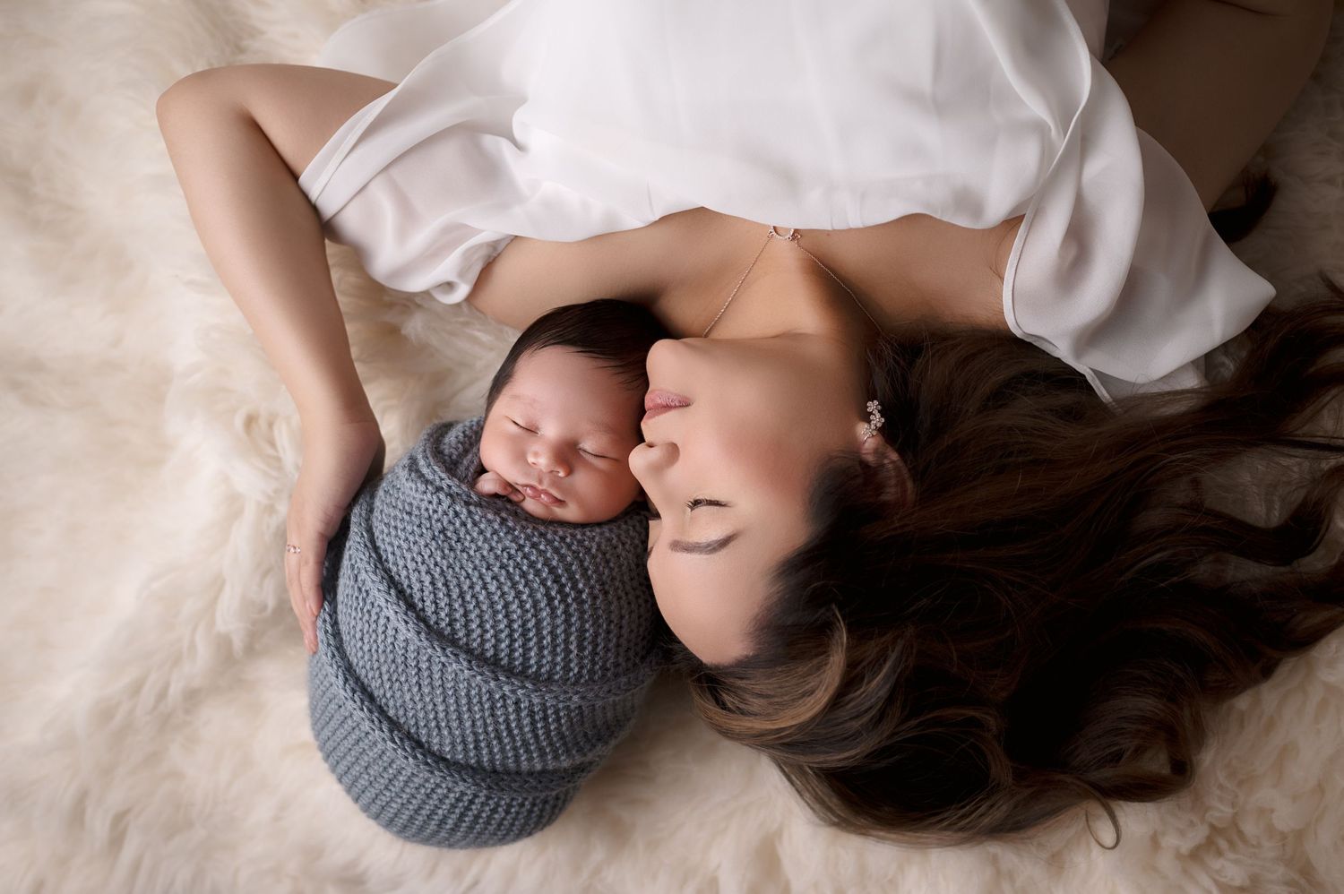 Mother and newborn in intimate pose on white backdrop with baby in gray knit wrap.
