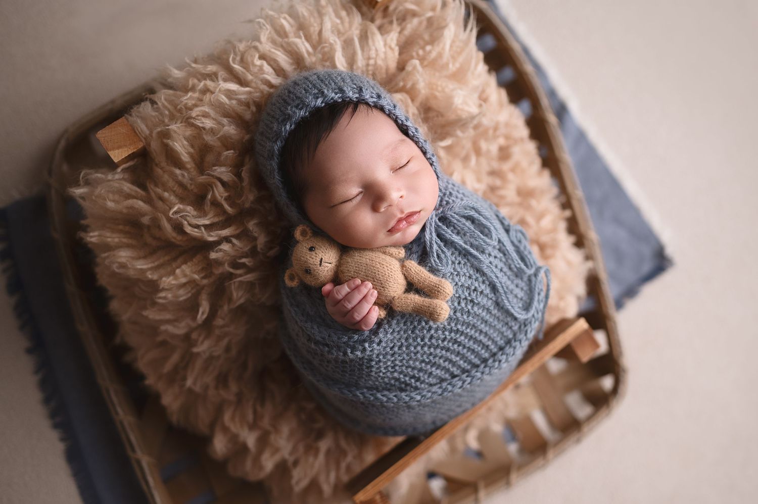 Newborn baby sleeping on fluffy rug wearing knit gray bonnet.
