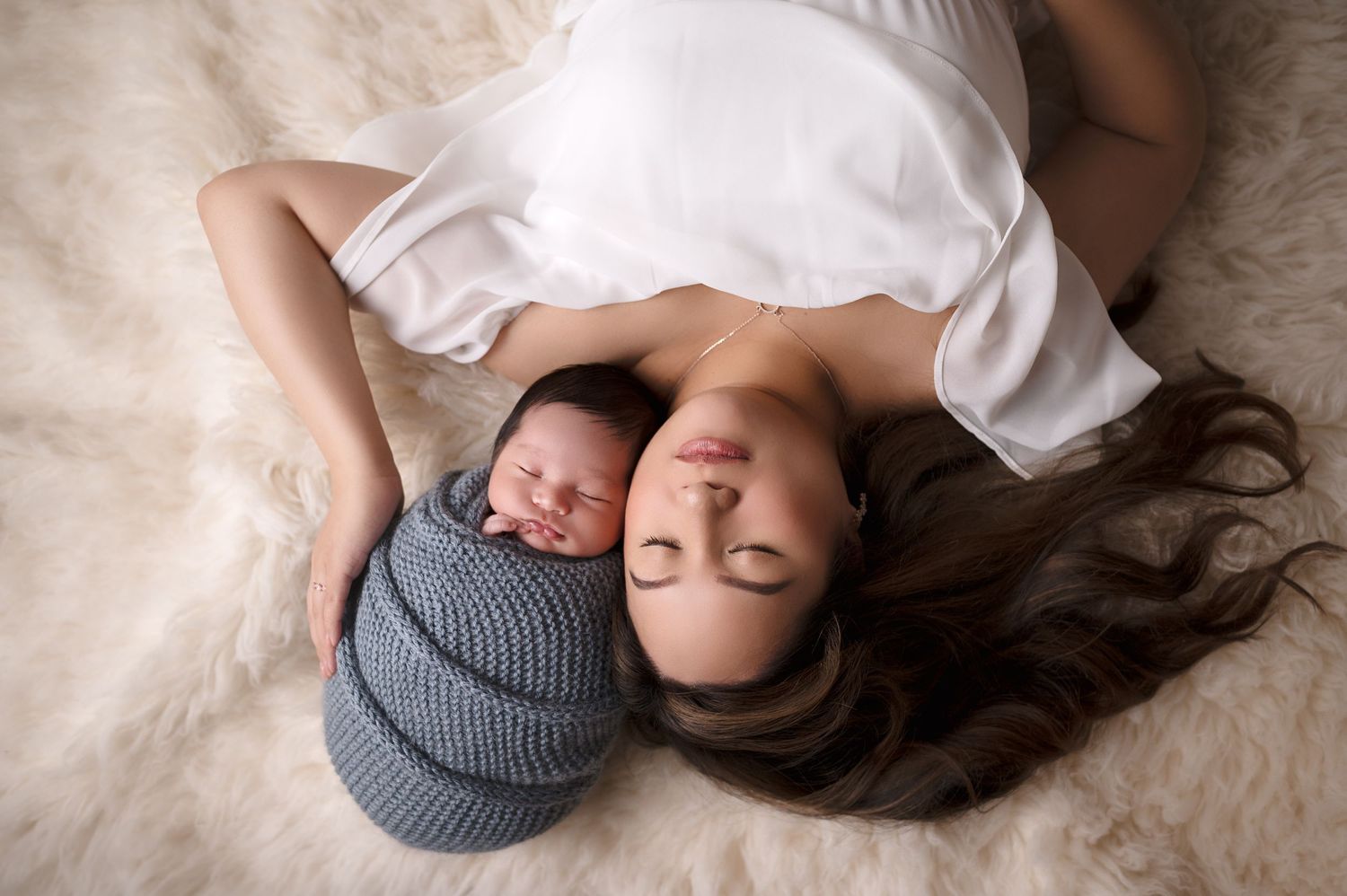 Baby rests on furry white blanket wearing cozy knit hat.