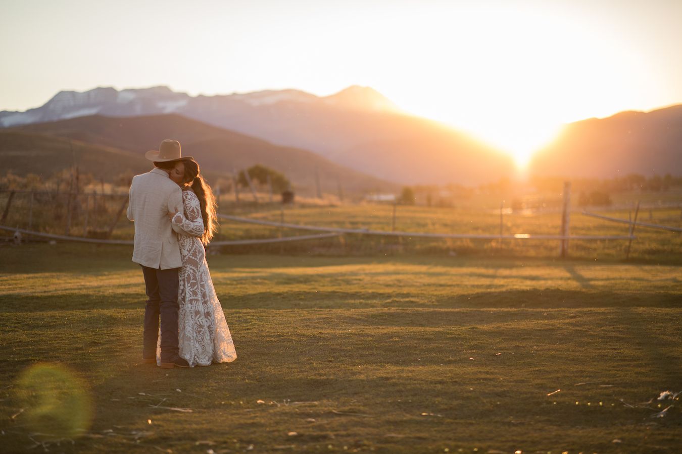 A romantic sunset photoshoot in a golden field with rolling hills and mountains in the background.