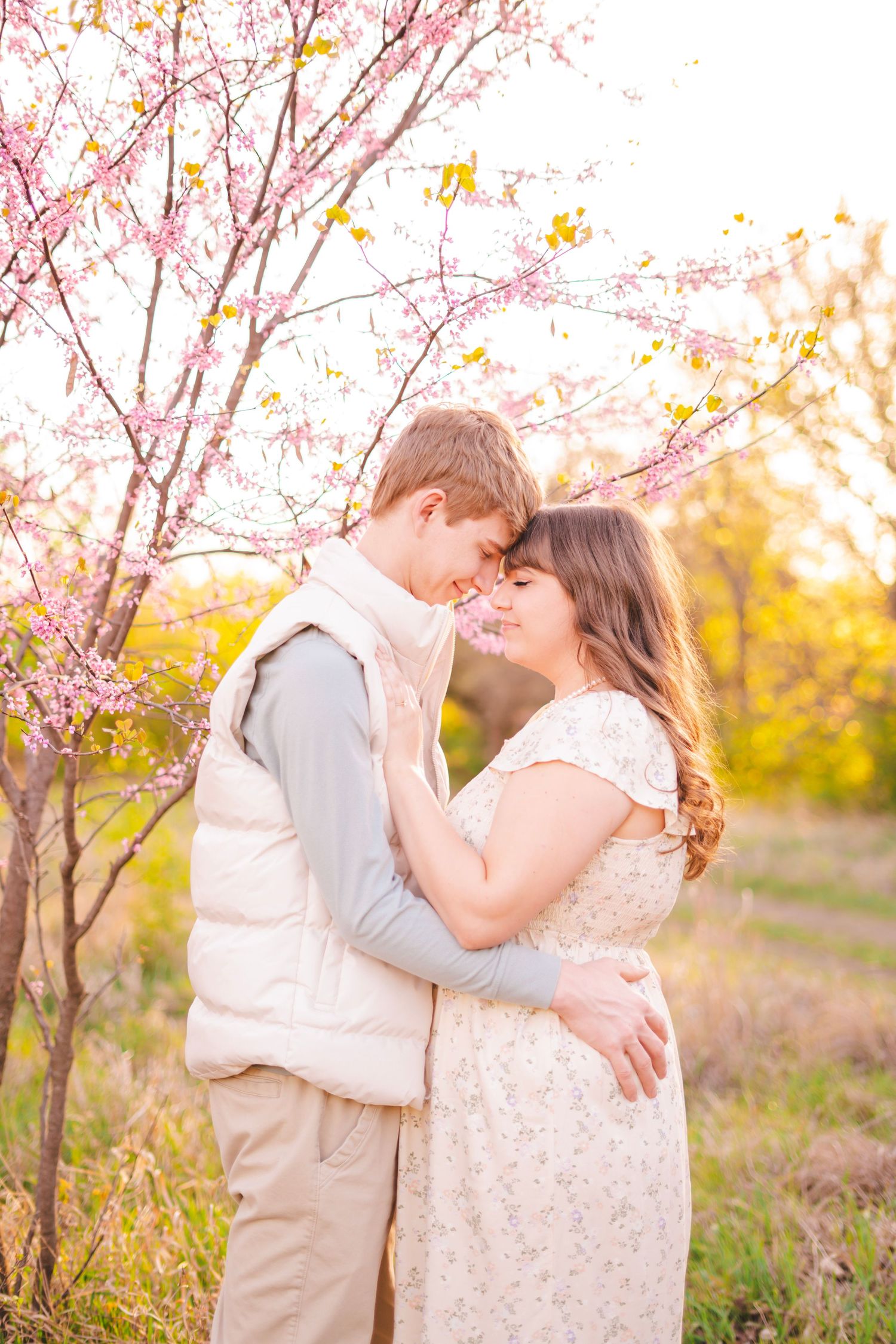 Romantic couple embracing forehead-to-forehead under blooming pink cherry blossom tree at golden sunset.