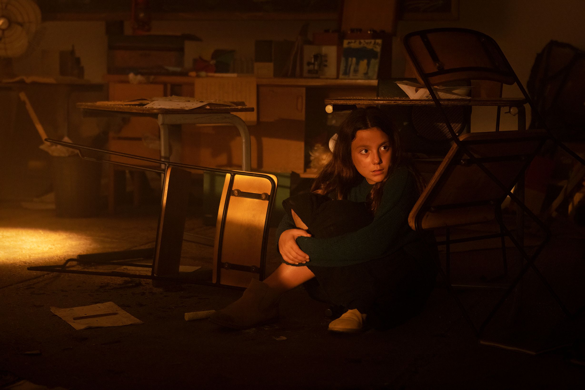 A young girl looks out from under a school desk on the set of a film.