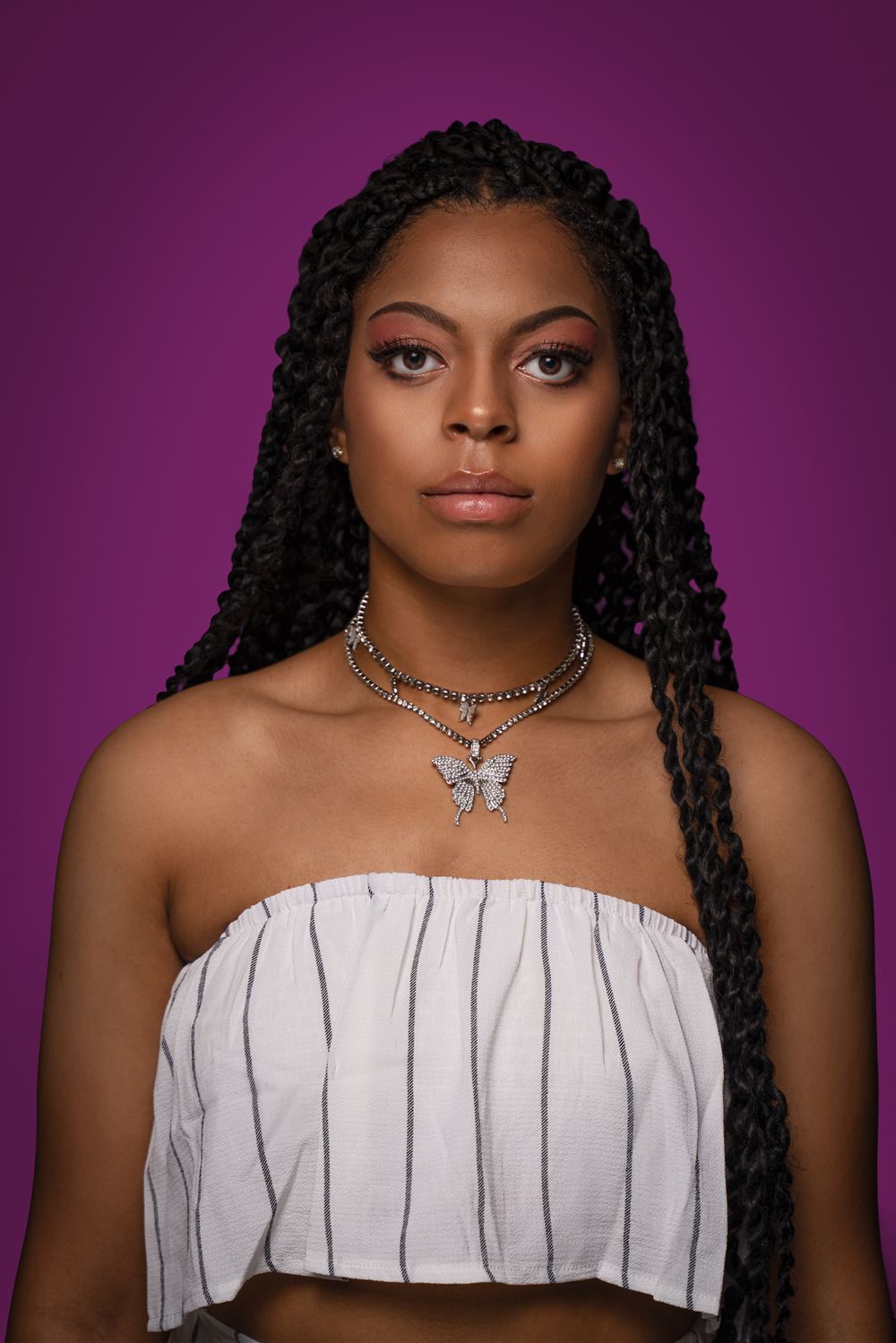 Portrait against purple background featuring white top and butterfly necklace.