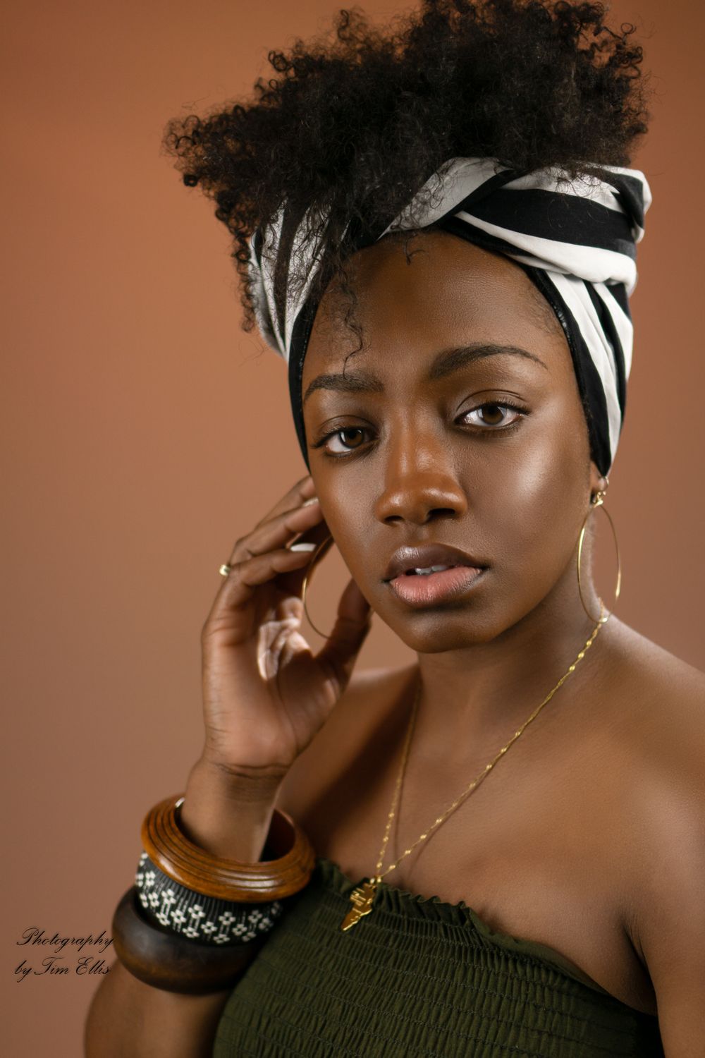 Portrait with warm lighting showing model wearing headwrap, jewelry and off-shoulder top.