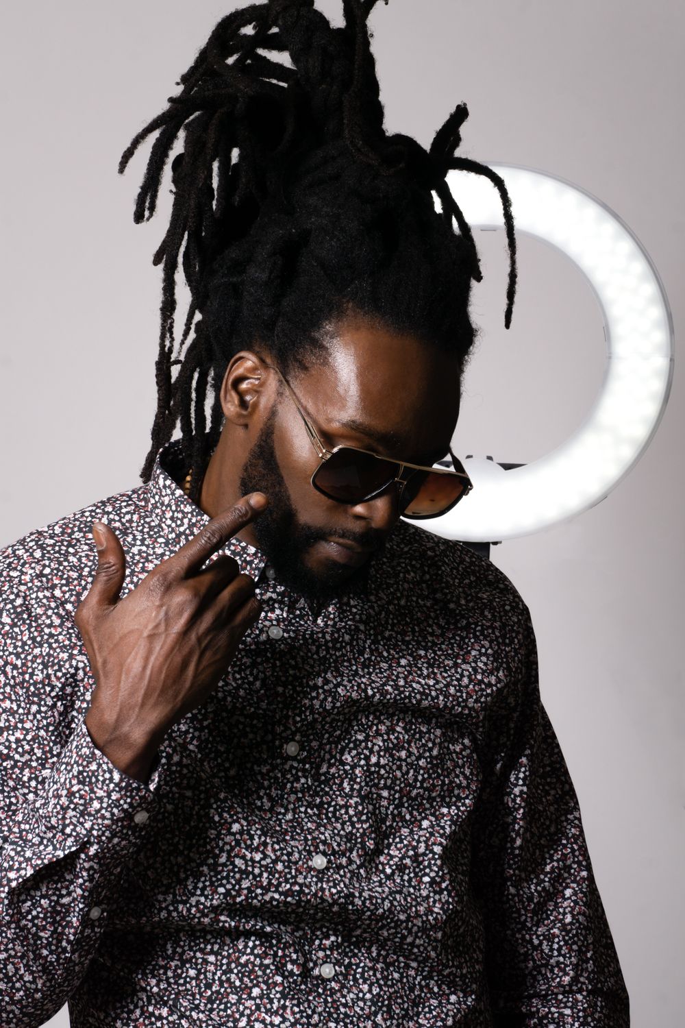 Studio portrait with dramatic lighting showing model in sparkly shirt with dreadlocks near illuminated crescent.