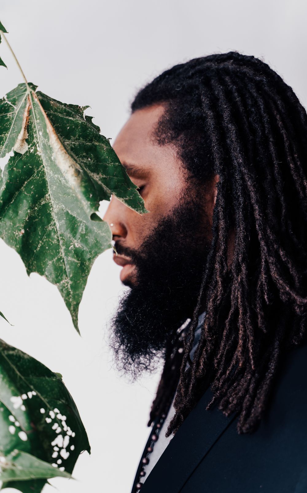 Artistic profile portrait with green leaf in foreground against white background.