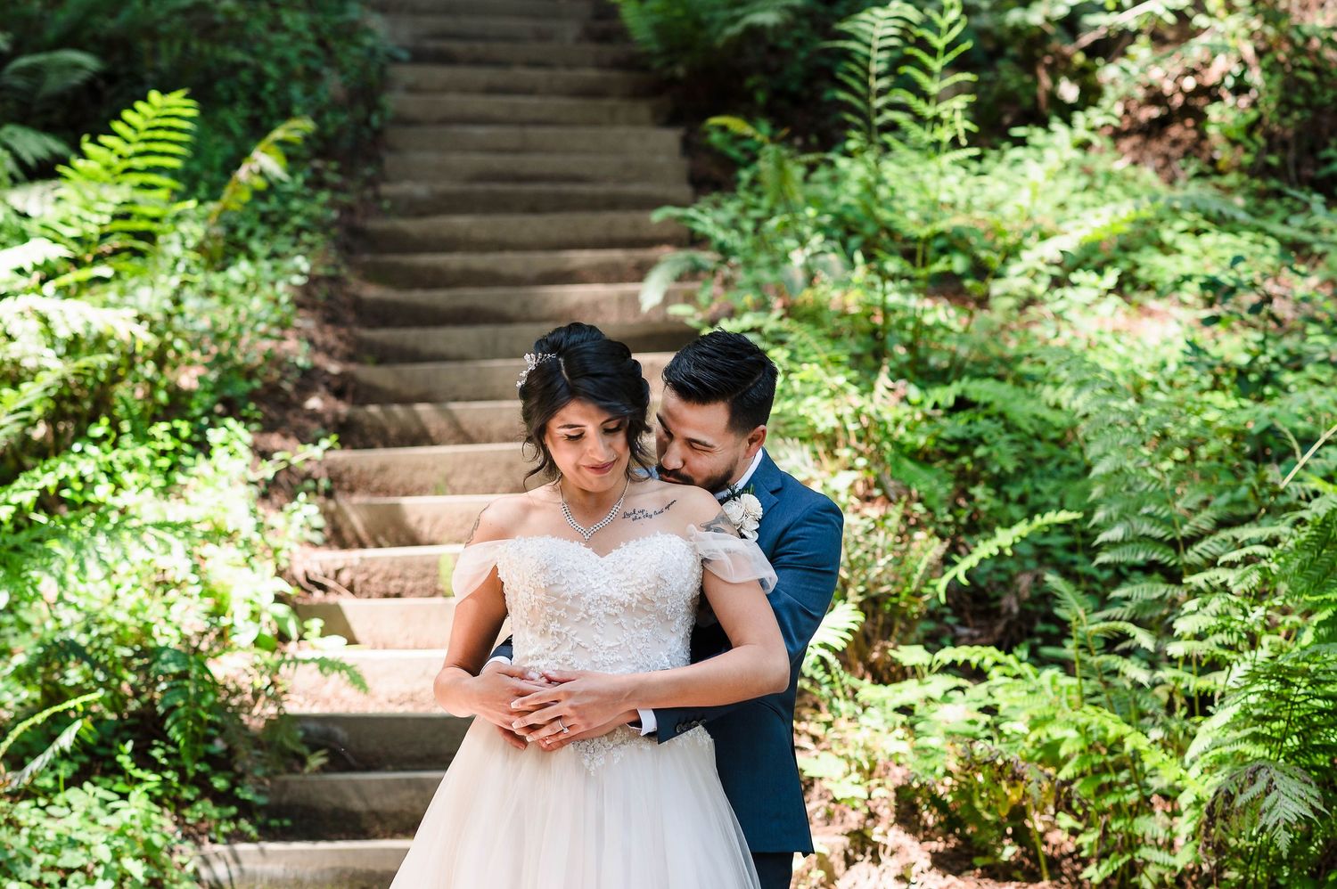 A tender moment shared on rustic stairs surrounded by lush forest ferns.