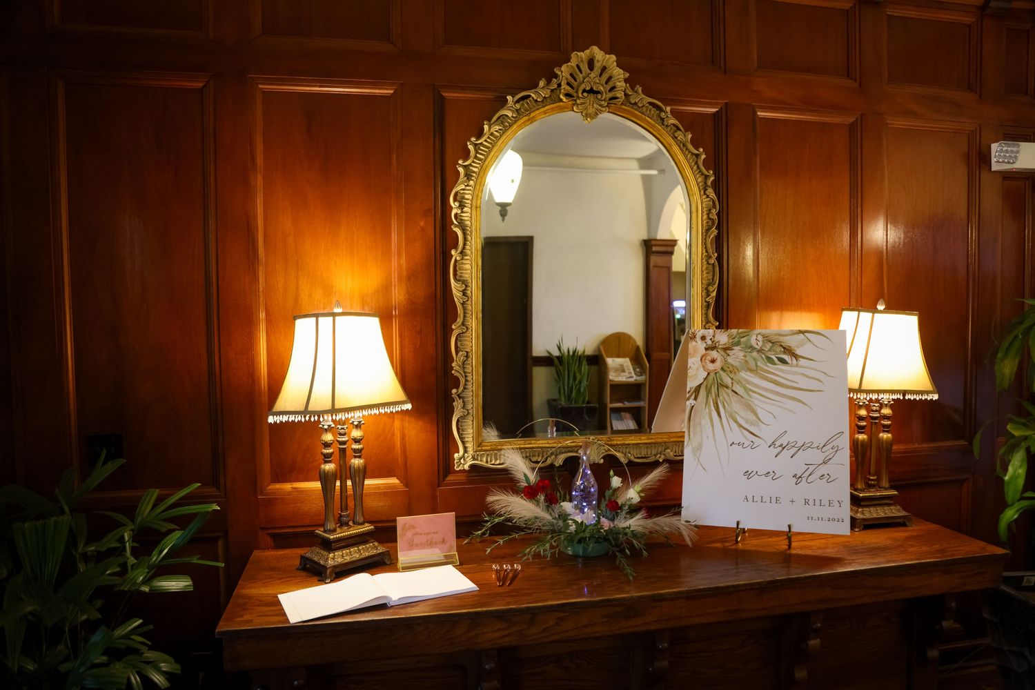 An elegant wood-paneled room with an ornate gold mirror flanked by table lamps.
