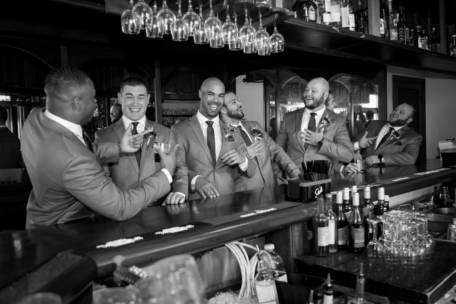 A vintage black and white scene of entertainers performing at a bar with hanging glassware above.