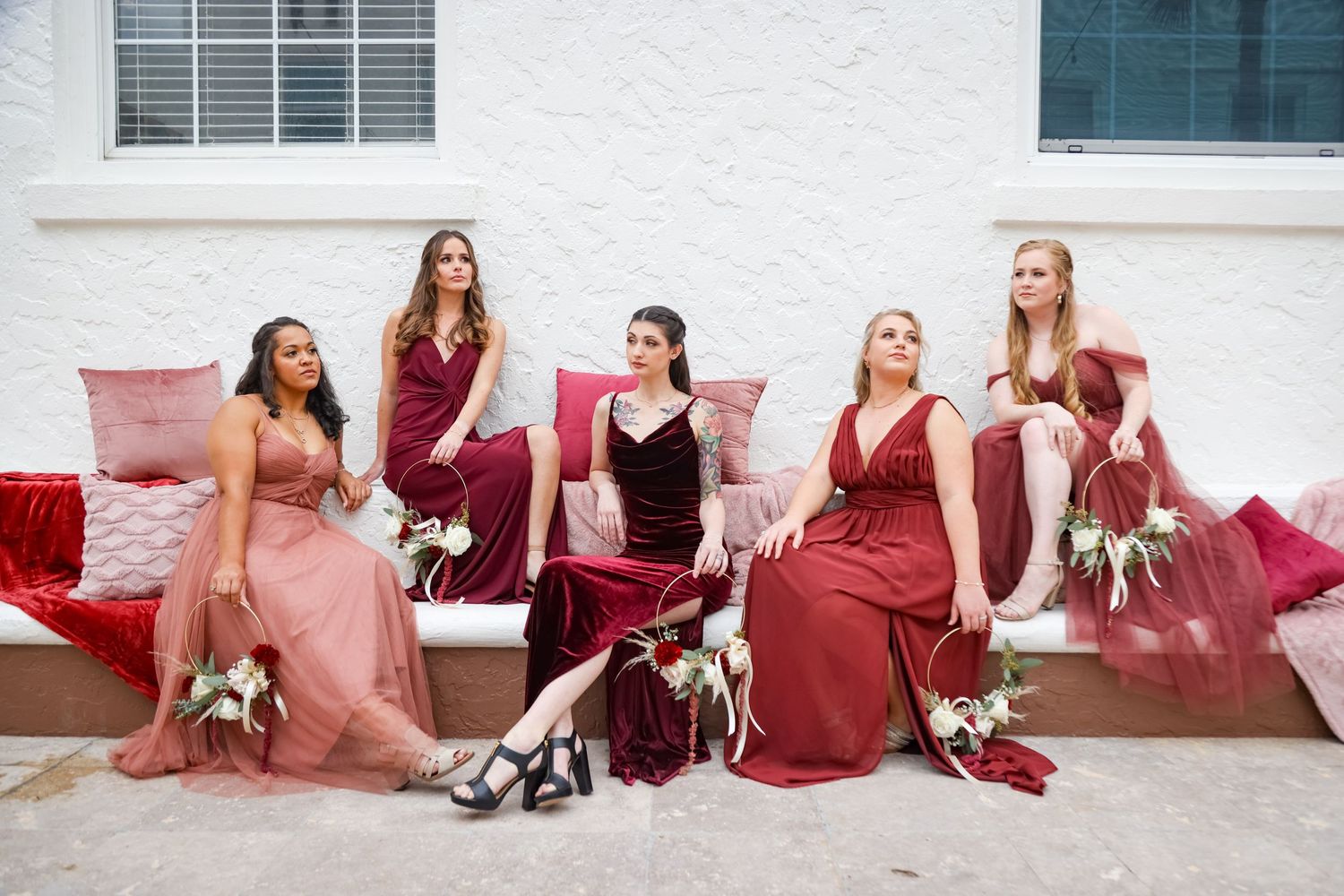 Wedding party in burgundy and blush dresses sits on pink seating with dogs at their feet on a cloudy day at Casa Marina