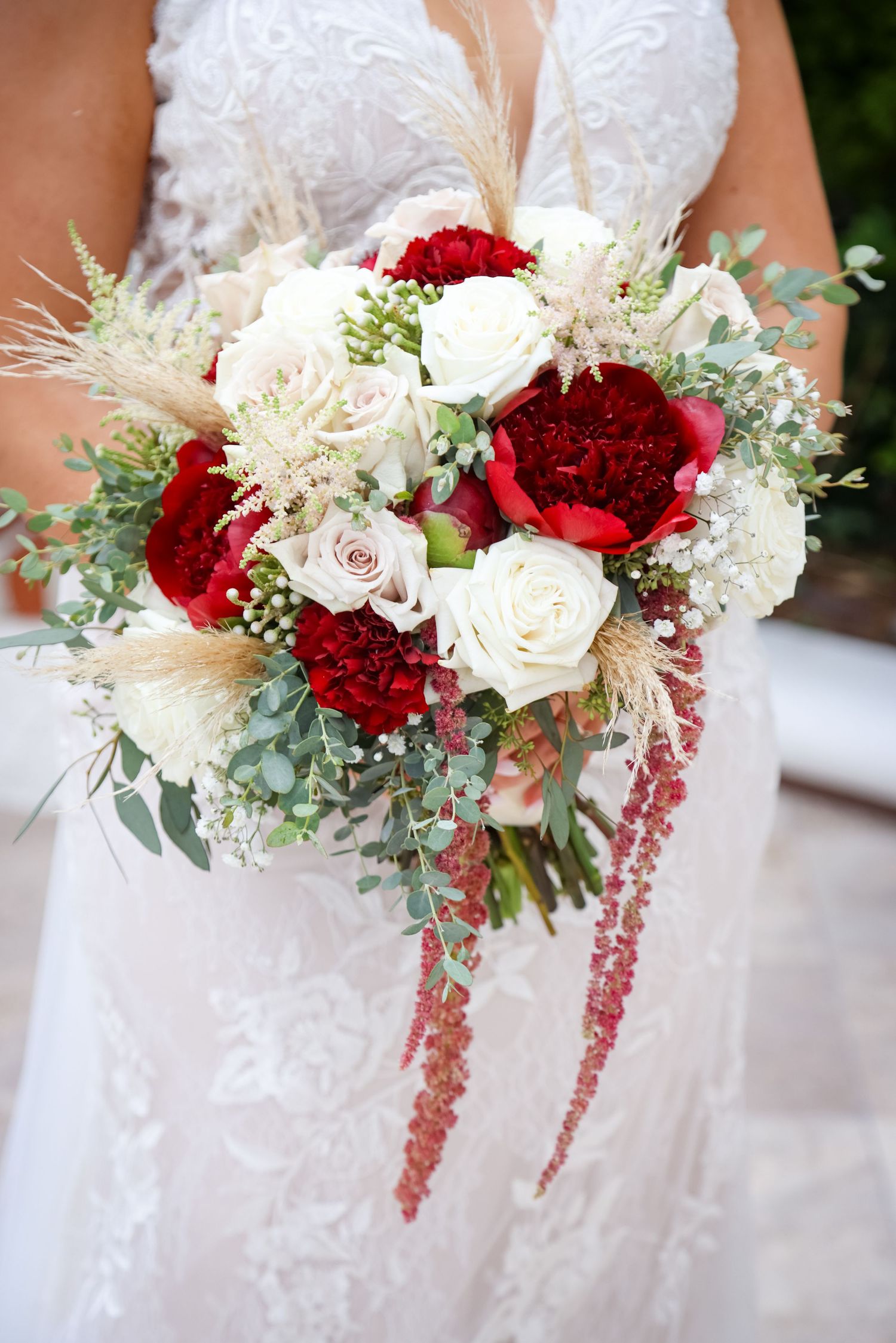 A romantic bridal bouquet featuring deep red and white roses with delicate pampas grass and eucalyptus accents.