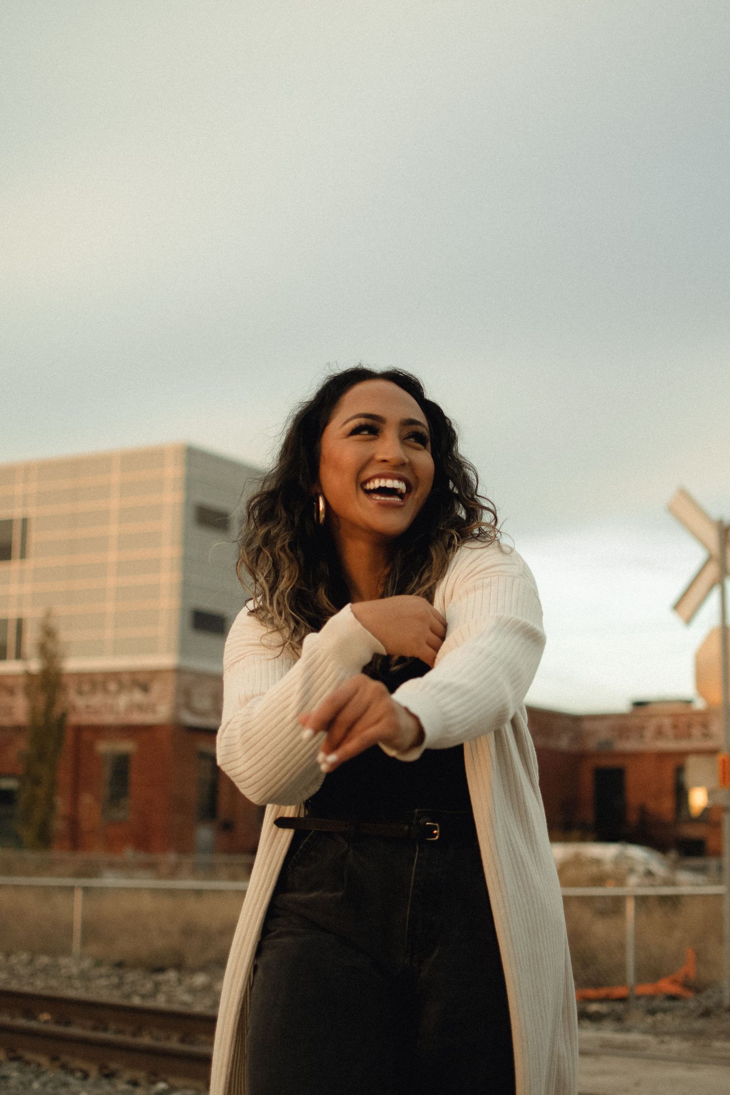 A joyful outdoor portrait near train tracks and urban buildings at golden hour.