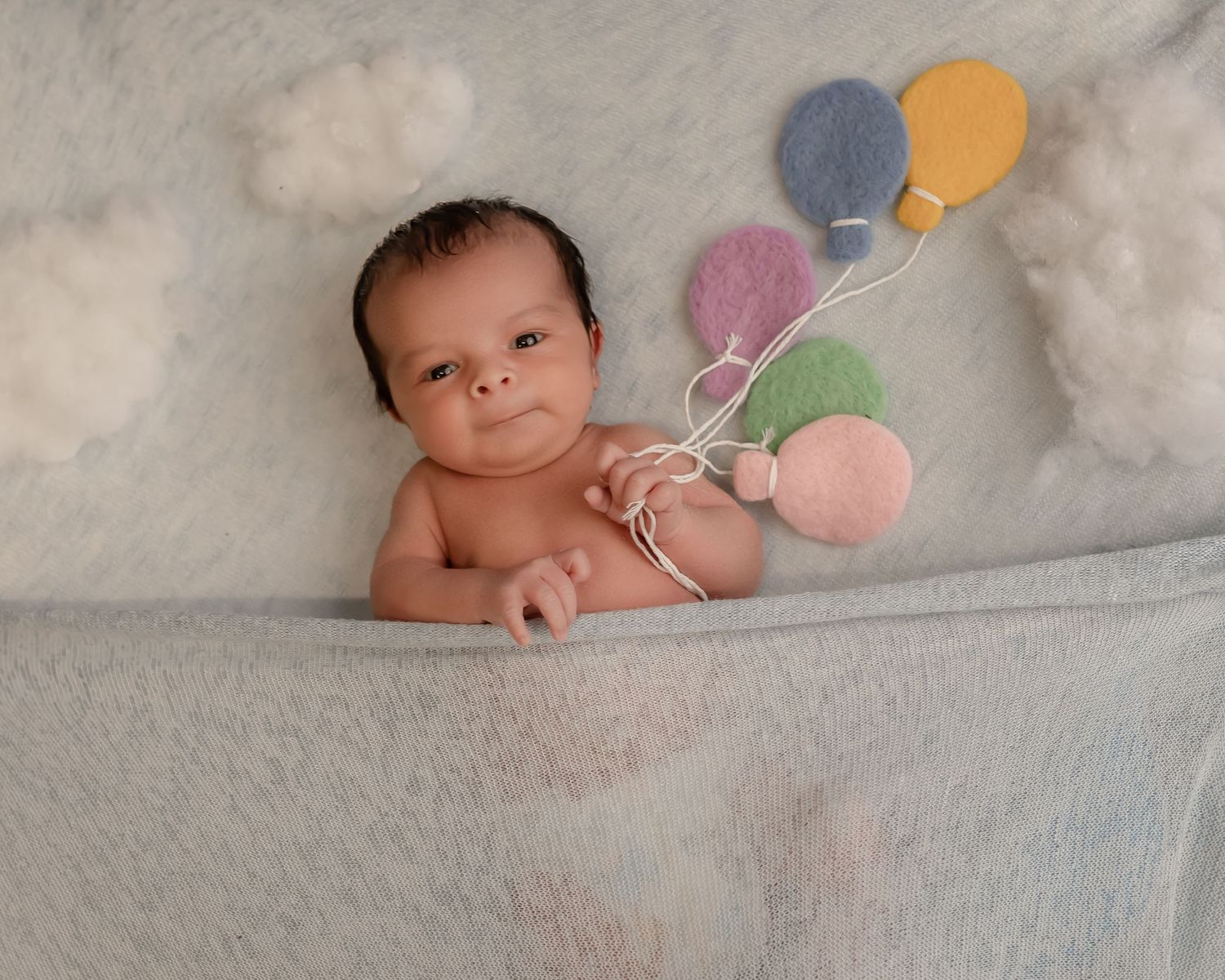 A newborn portrait with colorful balloon decorations against a soft white backdrop.