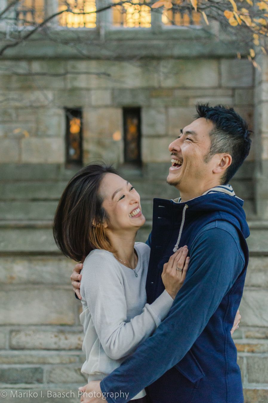 Happy Asian couple embracing and laughing together in front of a stone building.