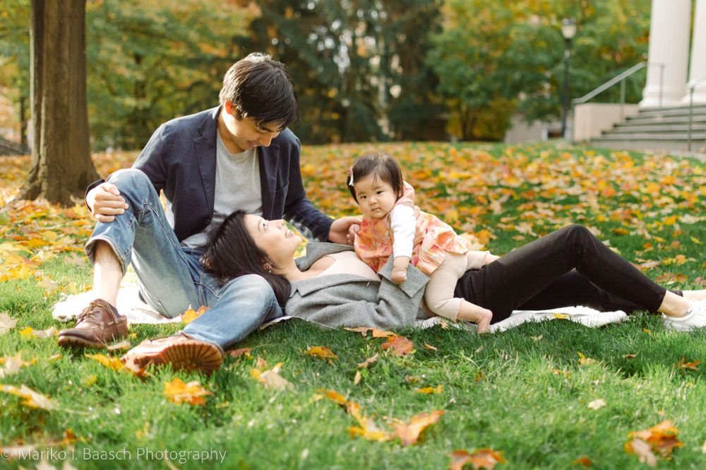 Asian family relaxing on grass covered in fall leaves with their baby girl.