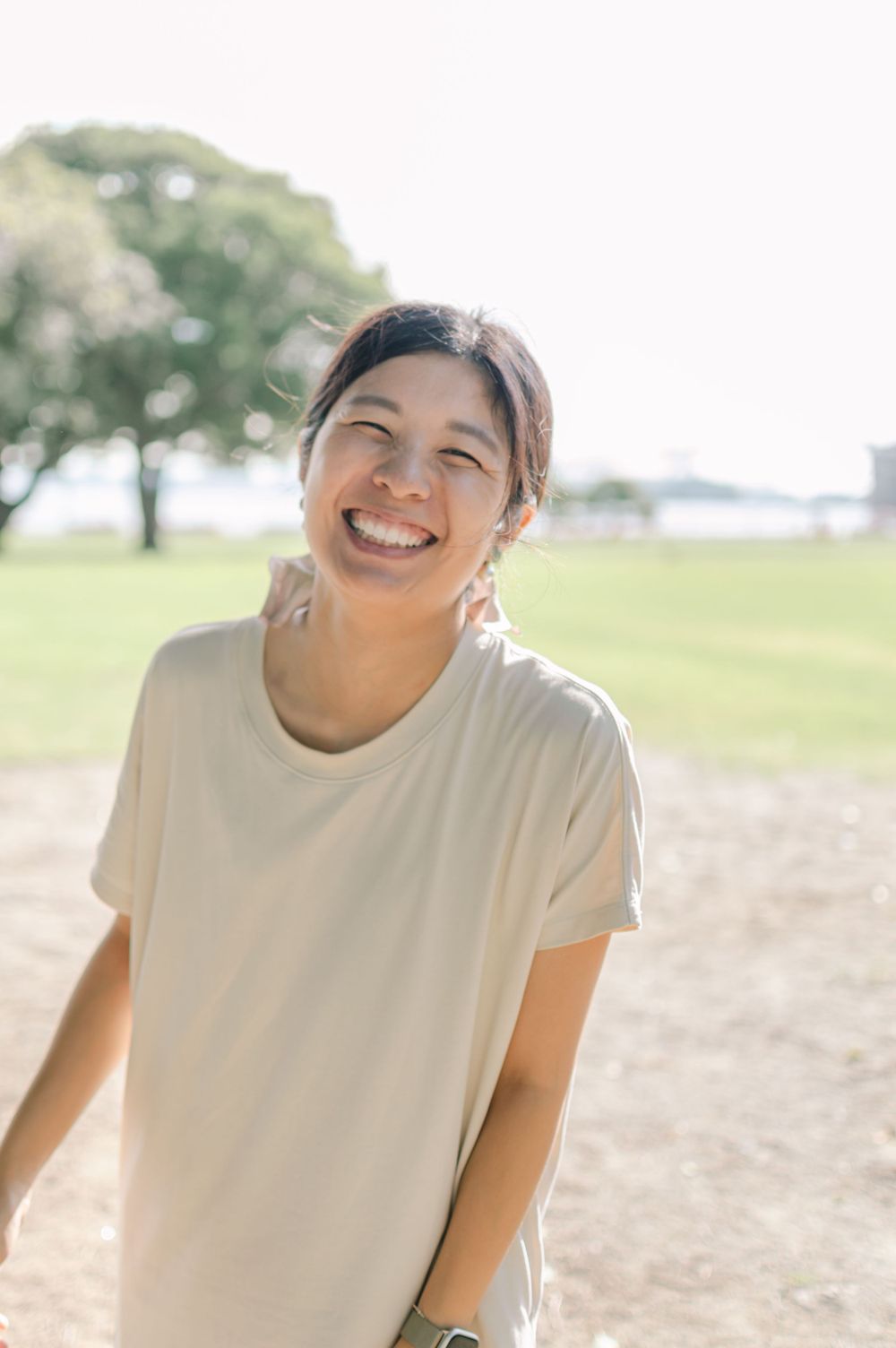 Joyful Asian woman smiling brightly in a sunlit outdoor park setting.
