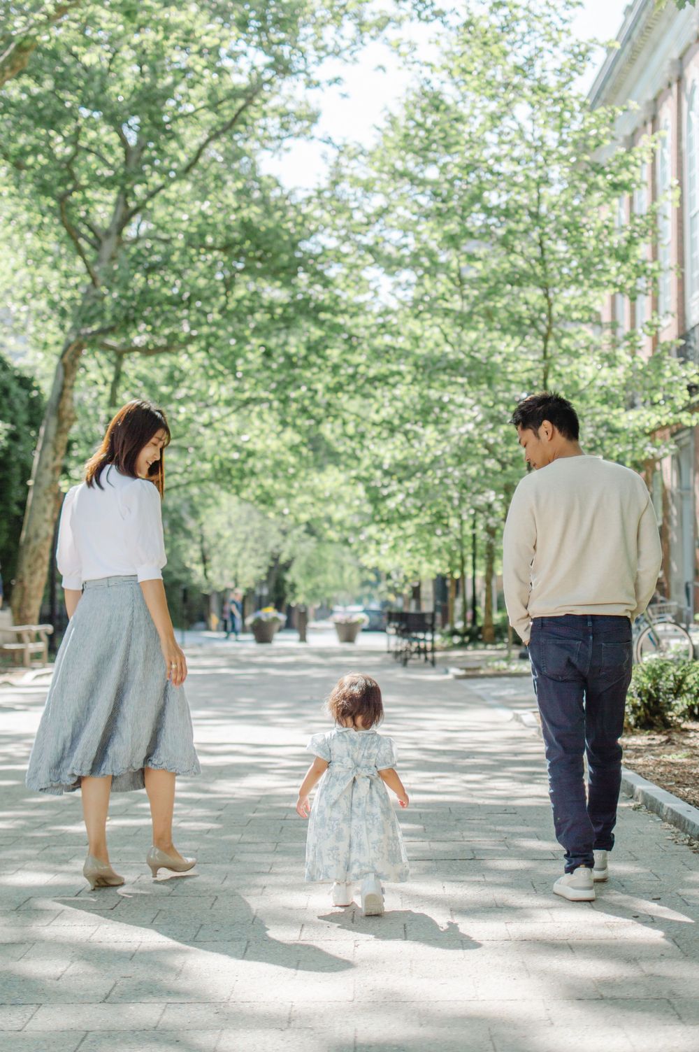 Family walking together on a tree-lined brick pathway with young toddler.