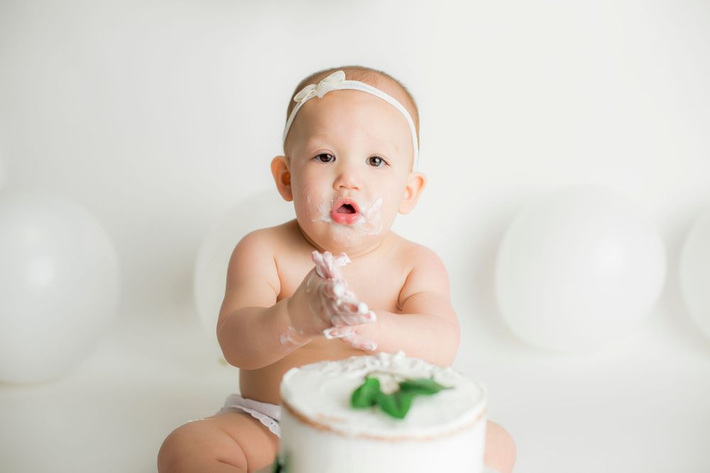 One year old baby girl sitting with her birthday cake infront of her looking at the camera.