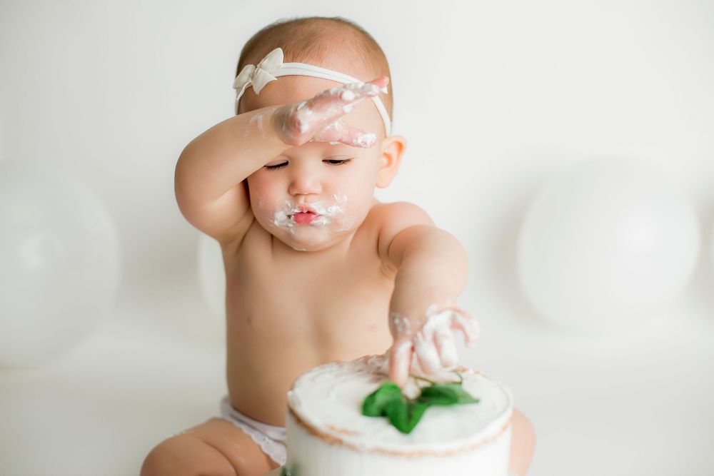 One year old baby girl wiping her head while eating her birthday cake.