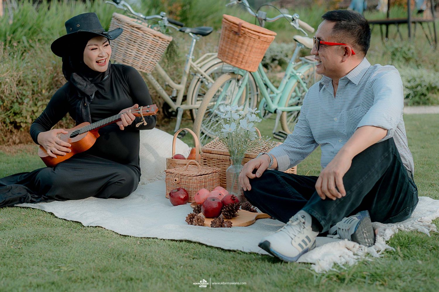 Couple enjoying picnic on lawn with vintage bicycles and ukulele.