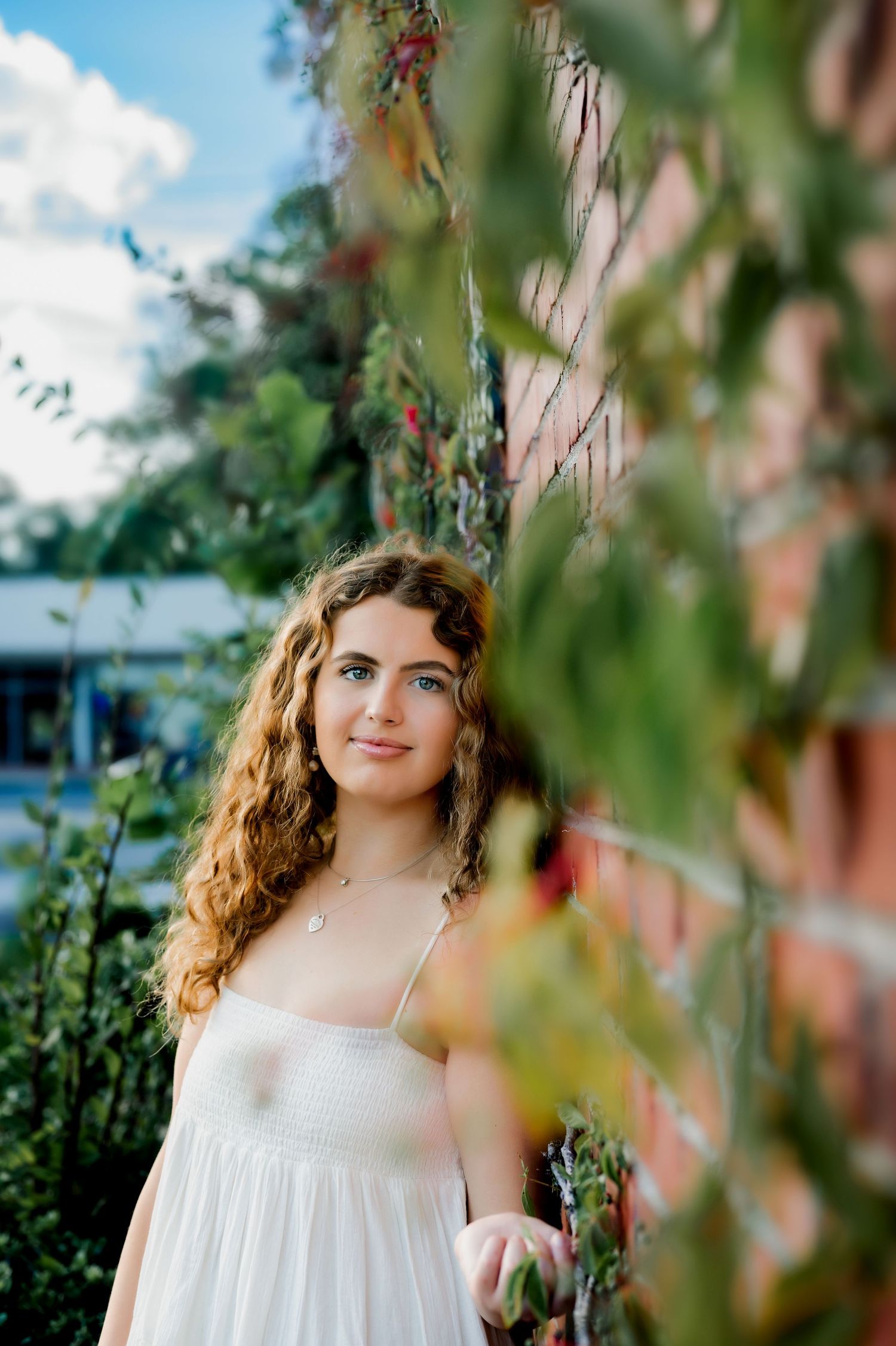 Portrait of woman in white dress framed by hanging garden foliage.