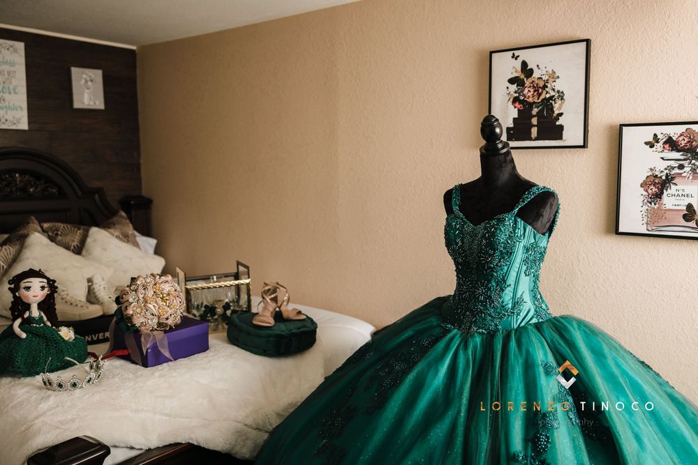 Emerald green quinceañera dress displayed on mannequin in bedroom setting.