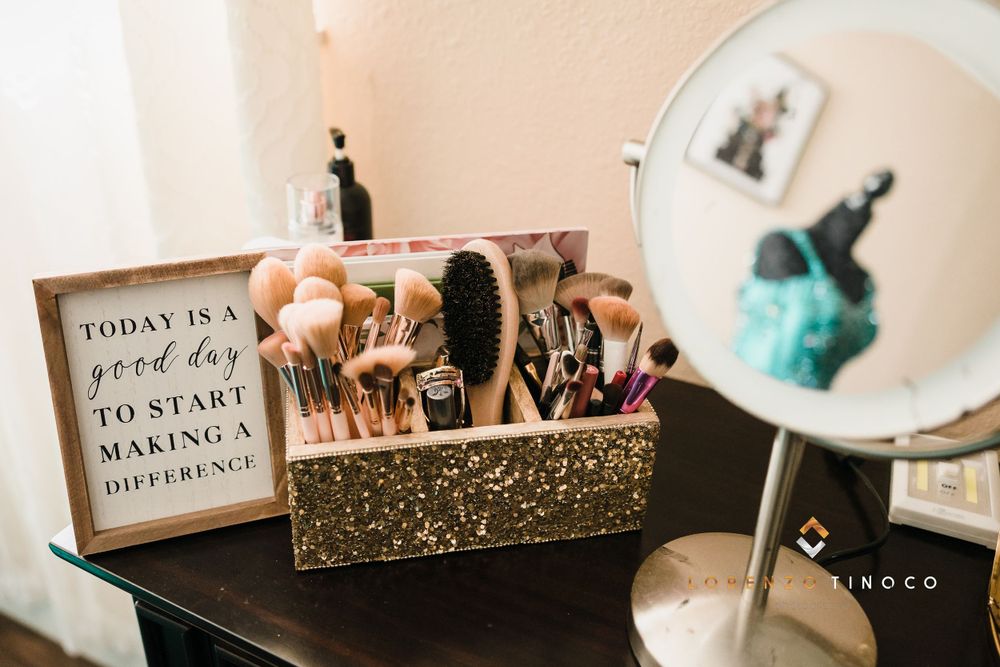 Makeup brushes displayed in glittery gold holder next to inspirational quote and vanity mirror.