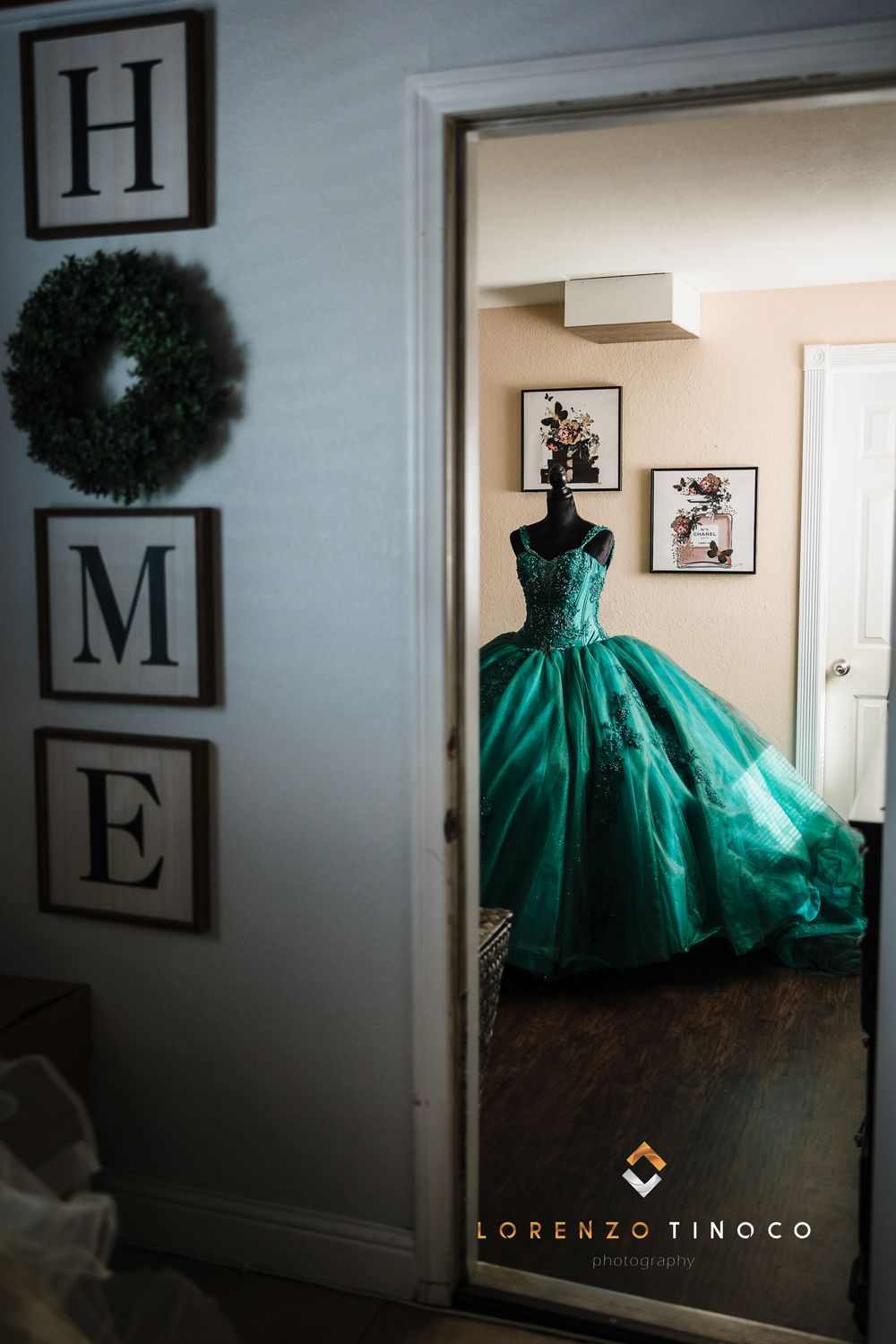 Elegant emerald green ball gown on display in doorway with HOME wall decor visible.