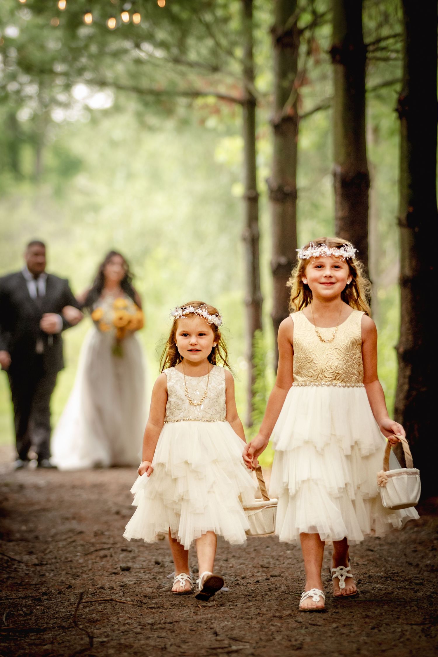 A brides daughters as her flower girls pictured walking together, leading the bride and her father down the aisle