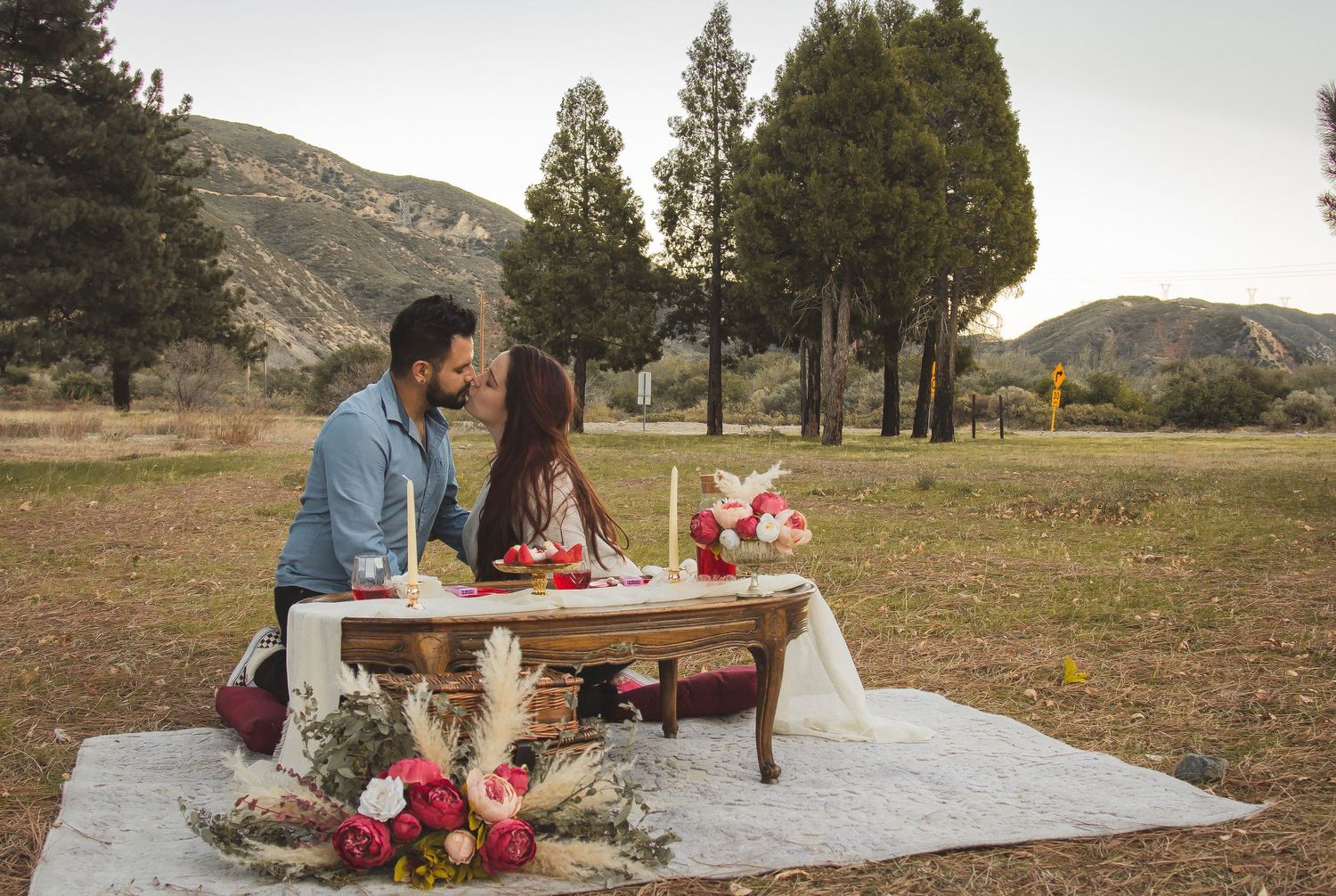 Romantic picnic setup with wooden table and flowers against mountain backdrop.