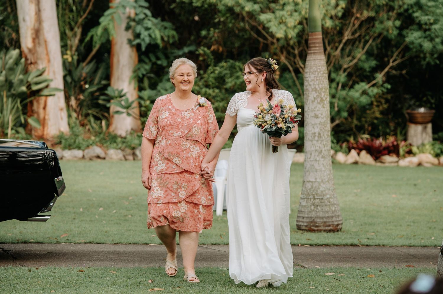 A touching wedding moment in a garden setting with palm trees and greenery.