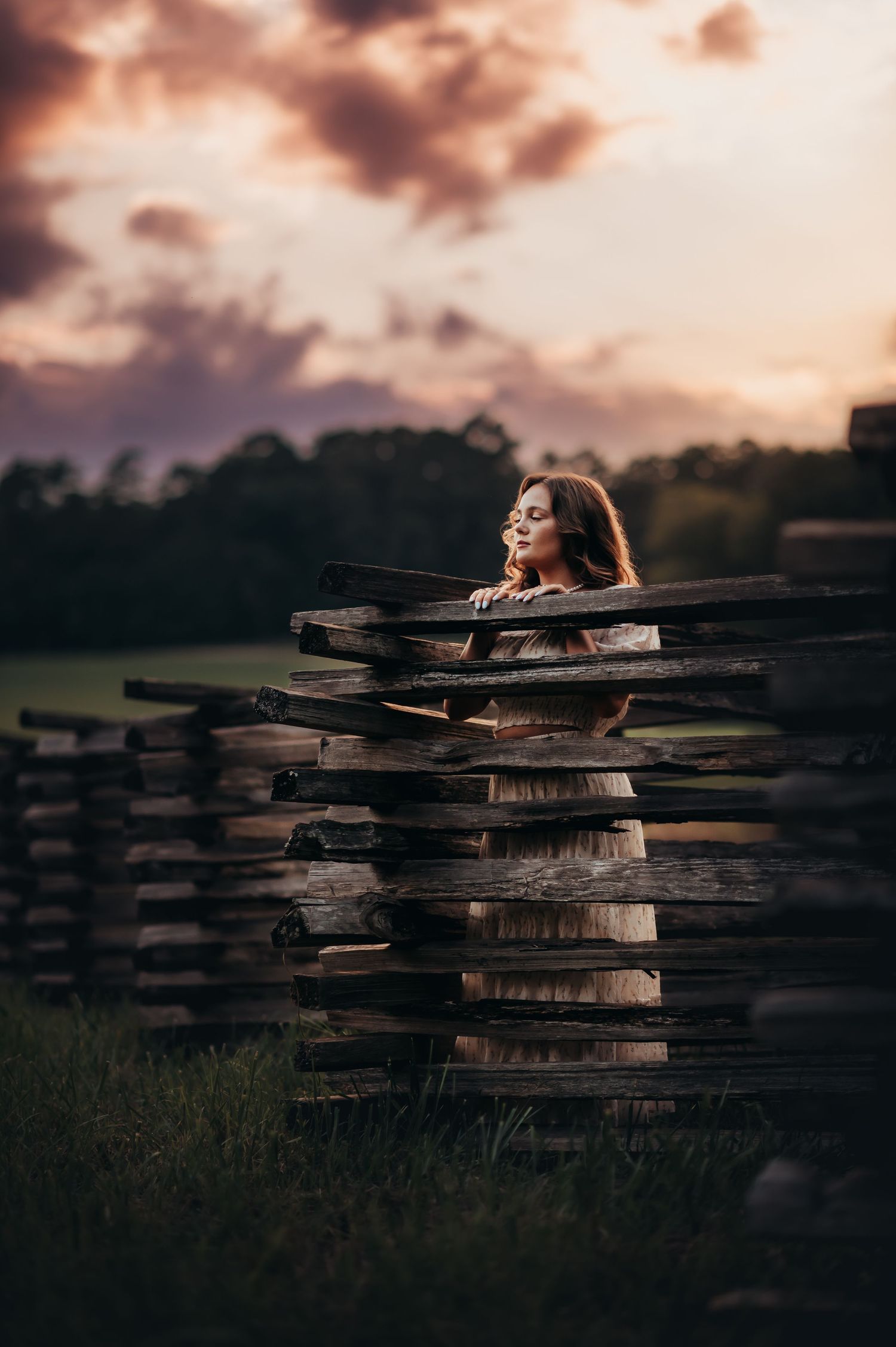 A woman leaning against one of the wooden fences of historic Chickamauga Battlefield at sunset with eyes closed..