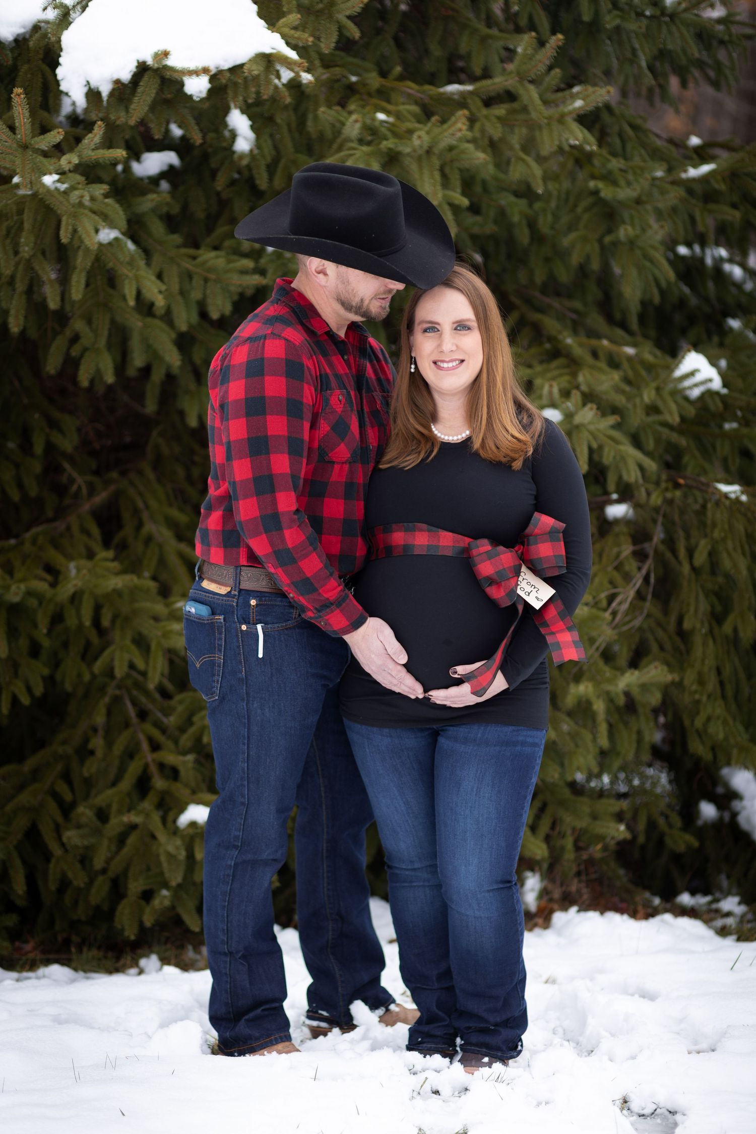 Soon to be parents holding the mom's pregnant belly while standing the the snow outside of Oblong, Illinois.