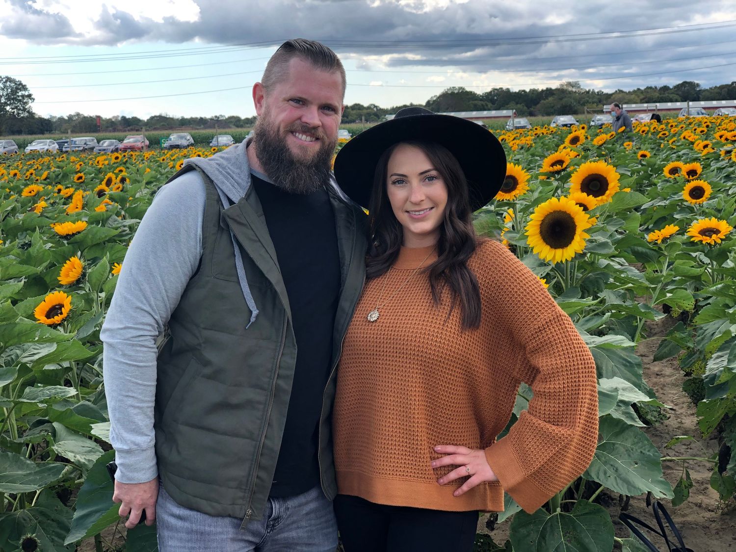 Couple posing together in vibrant sunflower field on cloudy day.