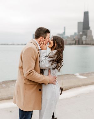 A couple embraces on the shores of Lake Michigan with Chicago's downtown skyline visible behind them.