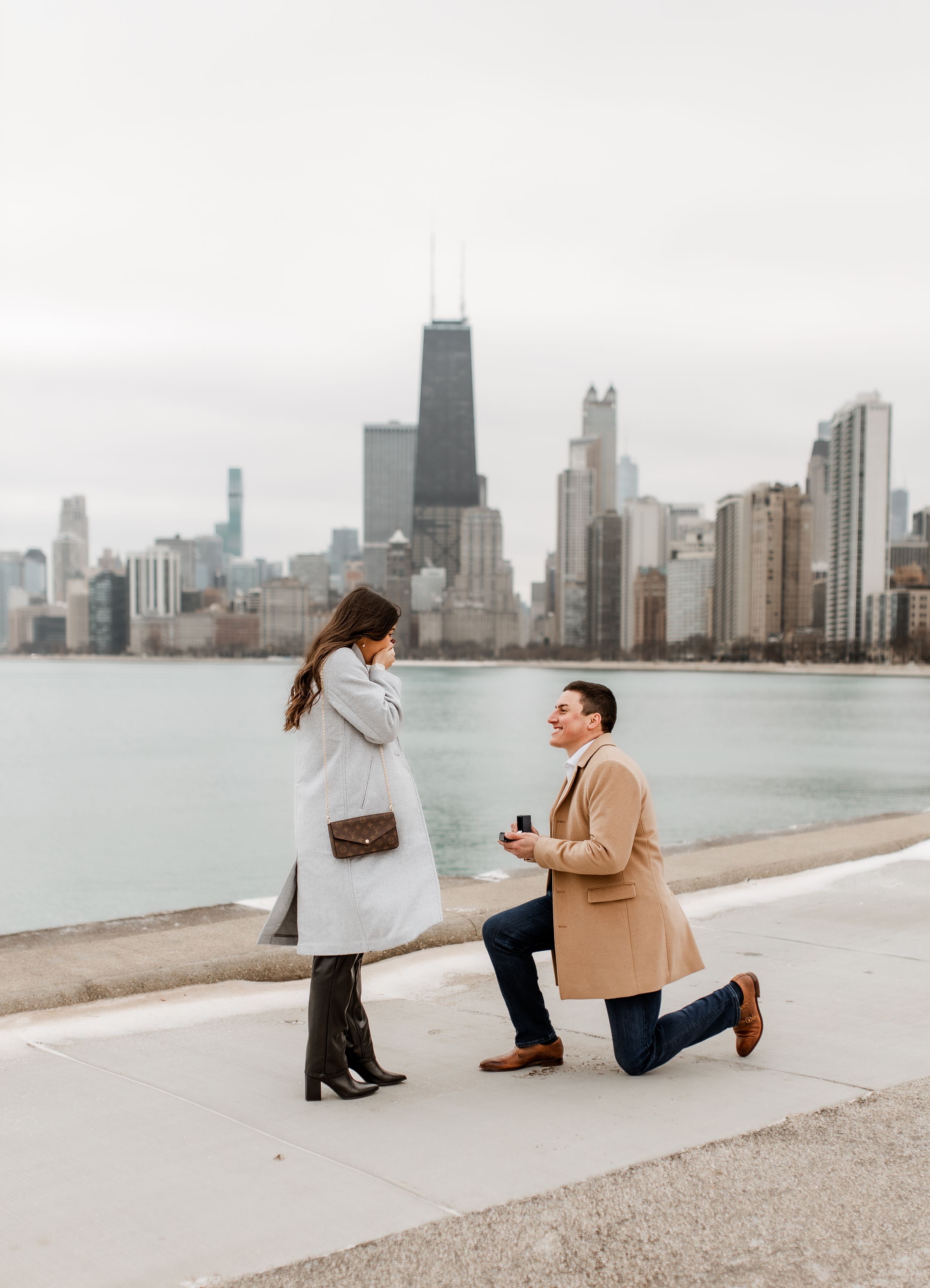 A proposal moment captured along Lake Michigan with the Chicago skyline creating a dramatic backdrop.