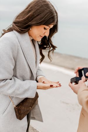 Woman in grey coat reacting to surprise proposal moment.
