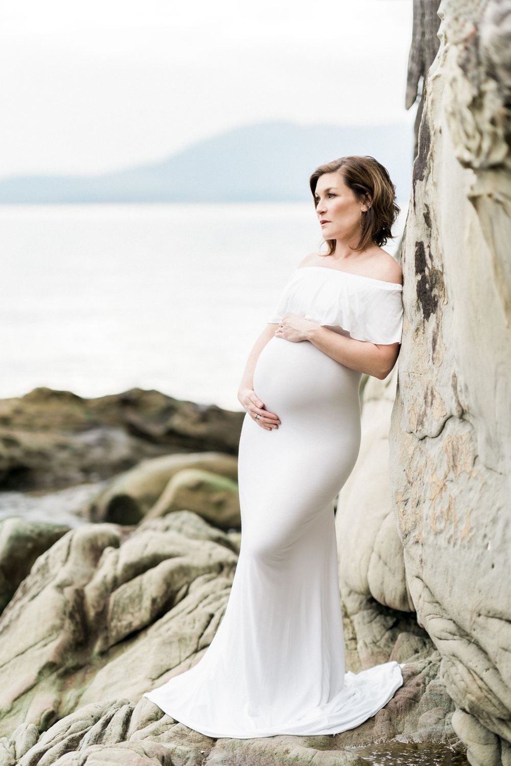Sandstone maternity session on the water in a white dress