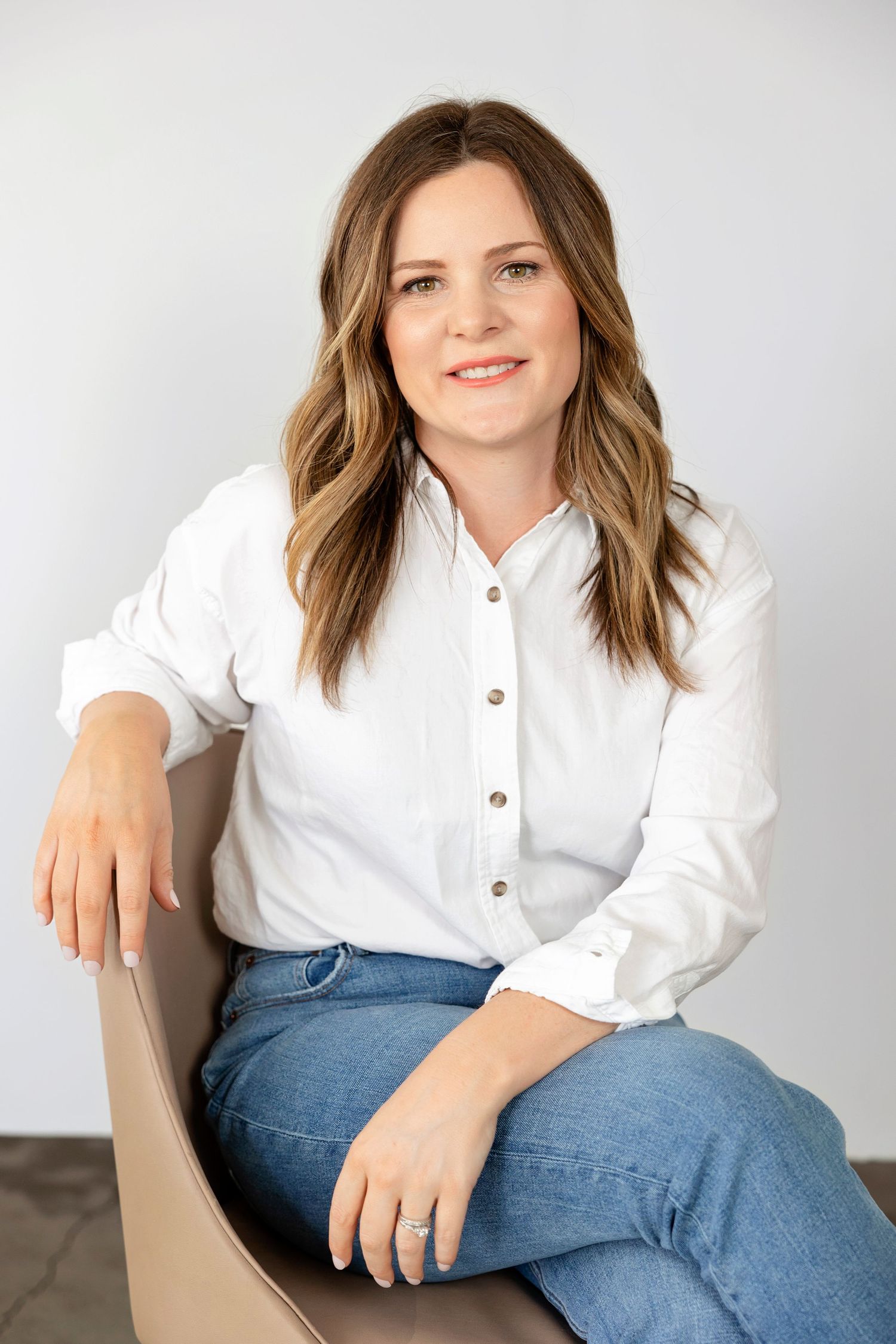 Professional portrait in white button-down shirt and jeans against neutral background.