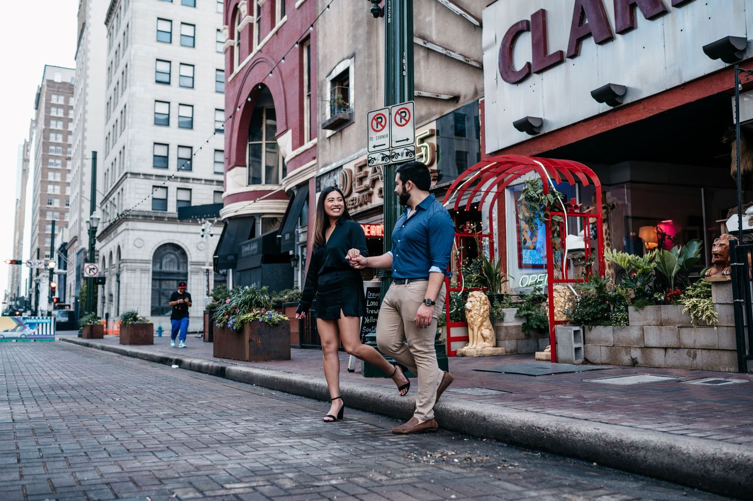 Couple walking together on a busy urban sidewalk past storefronts and restaurants in city setting.