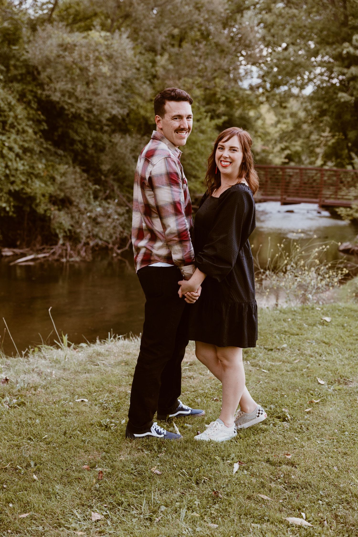 Happy couple posing together outdoors by a river in casual attire.