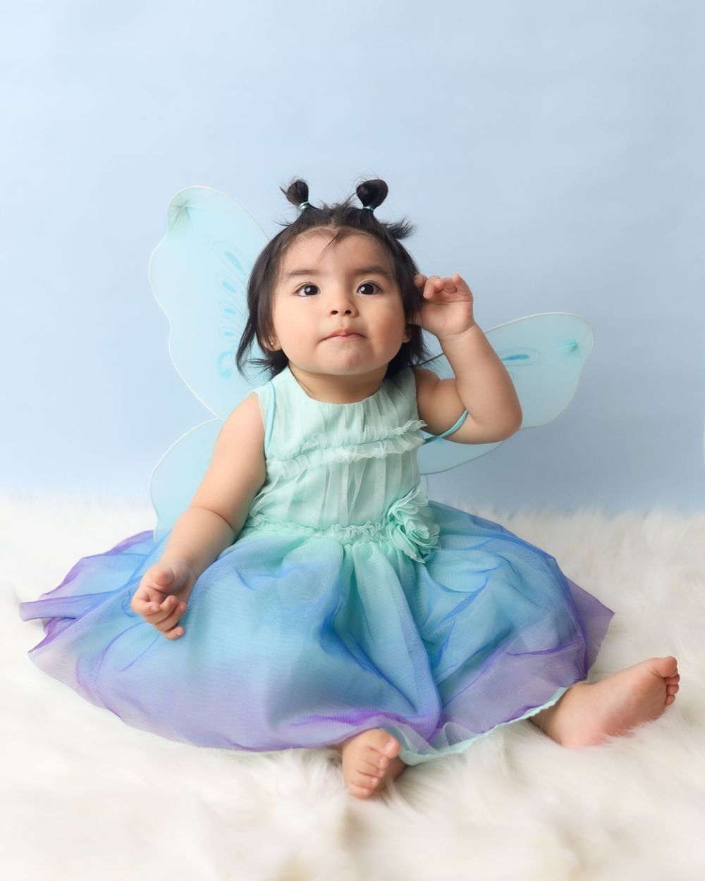 Baby wearing mint fairy costume with butterfly wings sitting on white floor.
