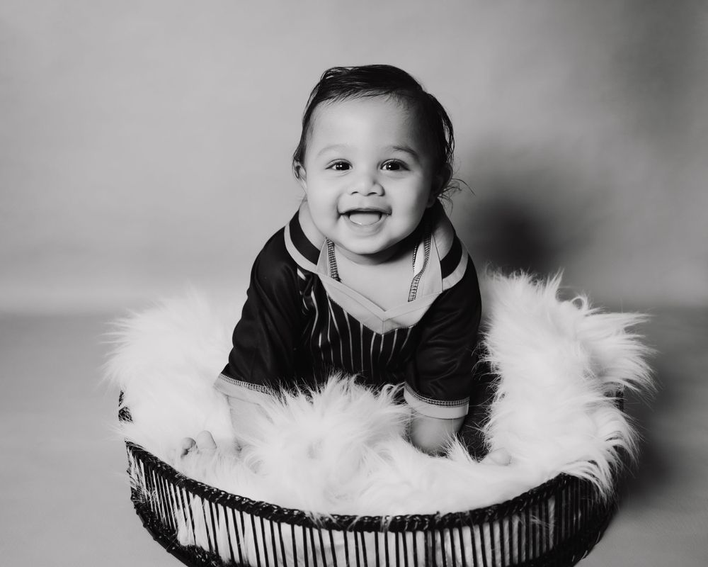Baby smiling in black outfit while sitting in furry basket.